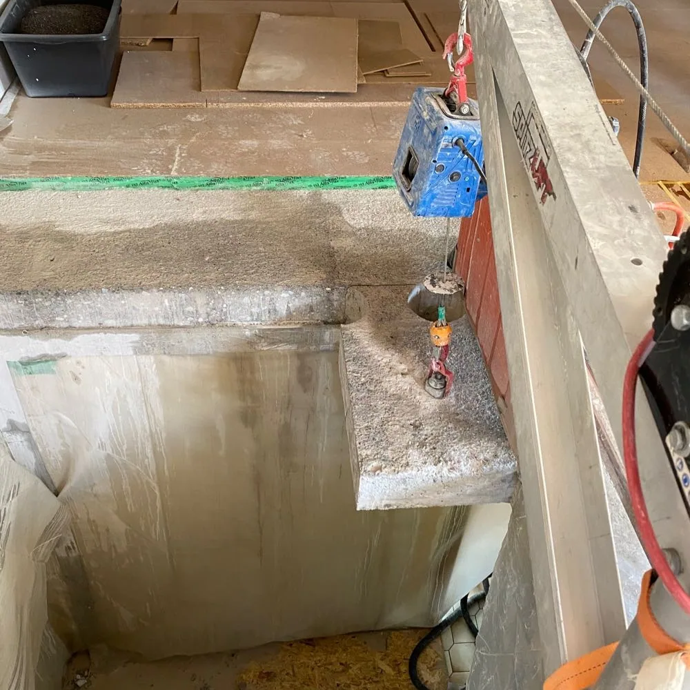 Ausgesägtes Betonteil hängt am Kettenzug des Spitzlifts über der Öffnung, darunter Folie und Schutzplatten