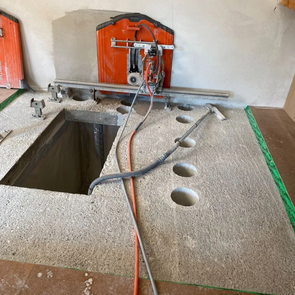 Wandsäge auf Führungsschiene an der Betondecke, daneben eine Reihe Kernbohrungen und der erste geöffnete Teil der Deckenöffnung