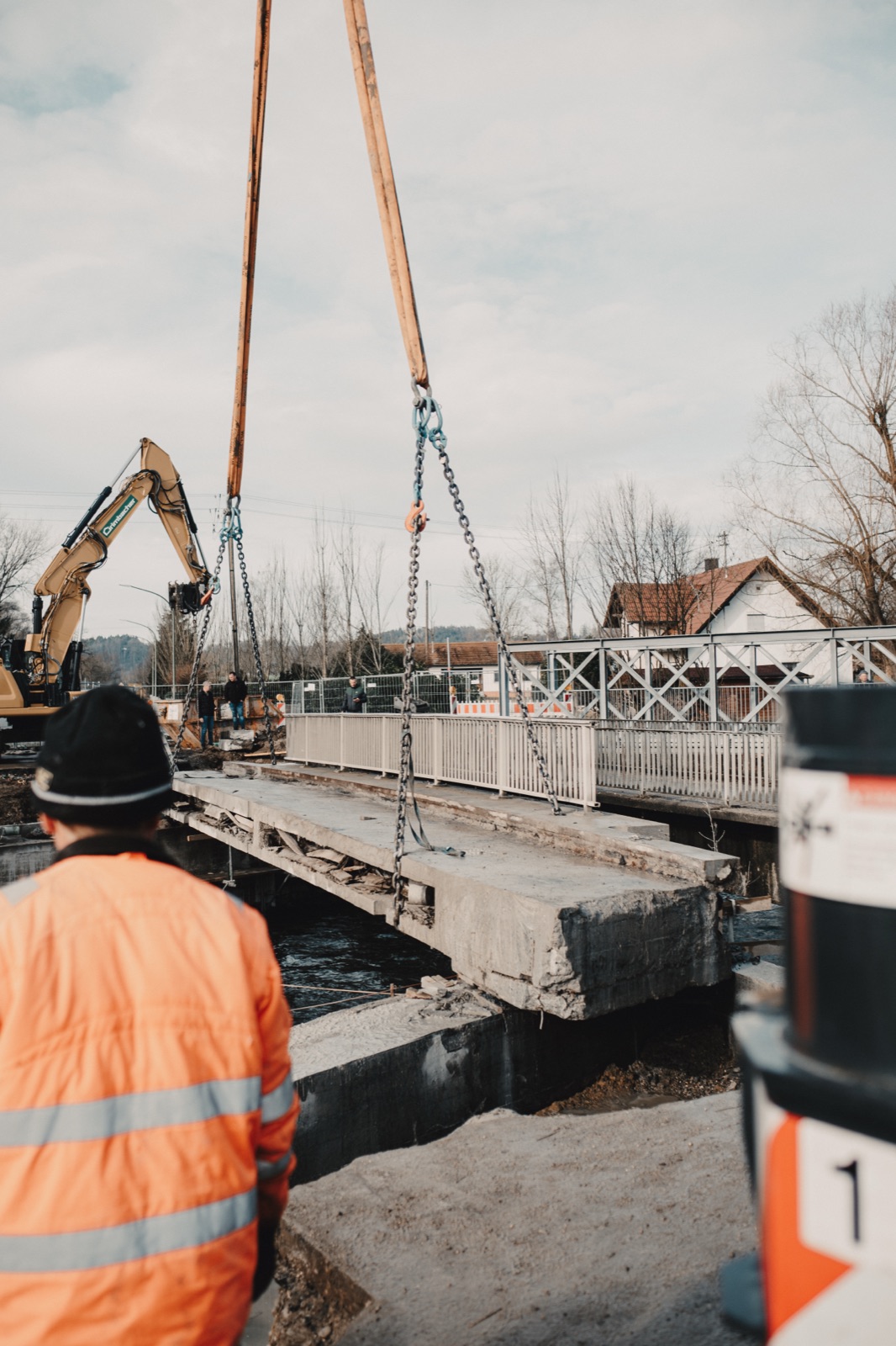 Fidan Monteur in orangener Warnweste beobachtet den Kranhub eines Brückenteils
